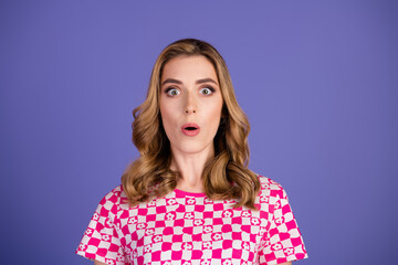 Surprised young woman wearing checkered t-shirt stands against violet background expressing...