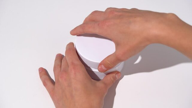 Female hands open a white jar with pink patches, take out a spatula on a white table background. Concept of beauty products under the eyes from dark circles, smoothing wrinkles, moisturizing.