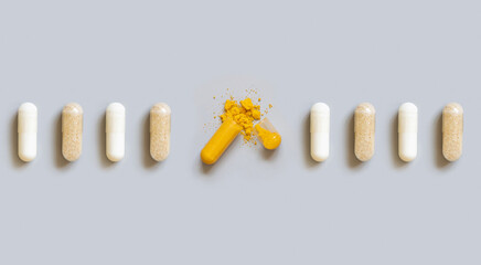 Beige medical capsules in a line with opened yellow one in the middle on grey top view
