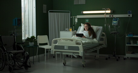 Patient in a hospital room uses a tablet while lying in bed.