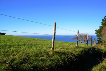 Fototapeta premium Valla de alambres y piquetes de madera en pradera de hierba verde junto al horizonte marino en Asturias