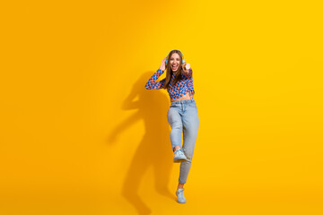 Young woman dancing joyfully with headphones, wearing stylish casual clothes and blue jeans against a vibrant yellow background