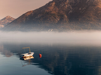 Small boat floating on calm water with misty mountains in background at sunrise