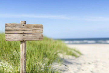 Naklejka premium rustic wooden signpost stands on sandy beach, surrounded by green grass and clear blue sky, evoking sense of tranquility and adventure