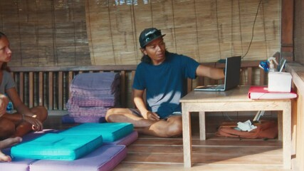 Asian teacher. Couple listening Indonesian man explaining something with laptop in a traditional Bali hut. Caucasian people attend lesson with asian teacher
