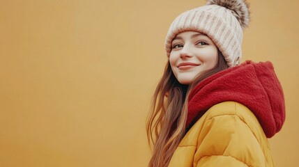Smiling young woman wearing a cozy winter hat and colorful jacket against a warm yellow background showcasing joyful winter fashion and comfort