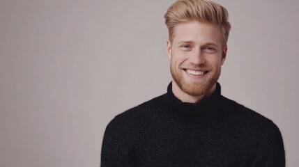 Obraz premium Smiling young adult man with stylish blonde hair and well-groomed beard wearing a cozy black woolen sweater against a neutral background