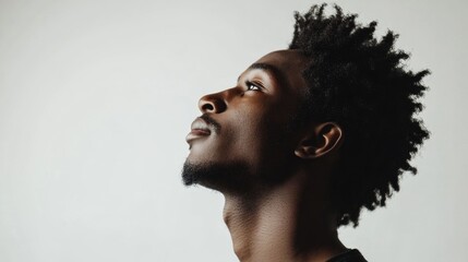 Profile view of young black man with textured afro hairstyle against a white background showcasing confidence and introspection in a studio setting.