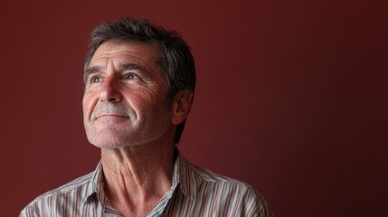 Obraz premium thoughtful 30-year-old man in colorful striped shirt gazing upwards with pensive expression against deep red textured background