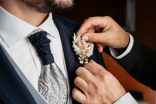 Manos de padrino poniendo el broche en la solapa al novio, preparativos el d&iacute;a de la boda