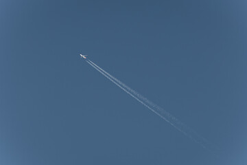 A high-flying airplane leaves a contrail across a clear, azure sky, showcasing the beauty of flight and the vastness of the atmosphere