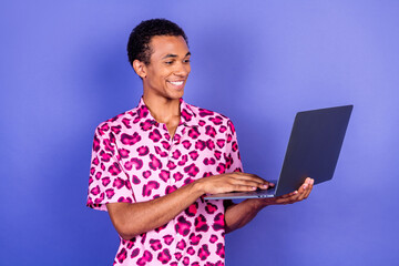 Young man with a trendy pink leopard-print shirt holding a laptop against a vibrant purple background