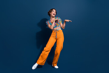 Full length photo of lovely young lady dancing have fun funky dressed stylish flared pants isolated on dark blue color background