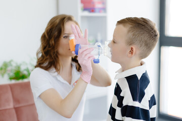 Boy with allergic asthma, inhaling his medication through spacer while sitting in doctors office