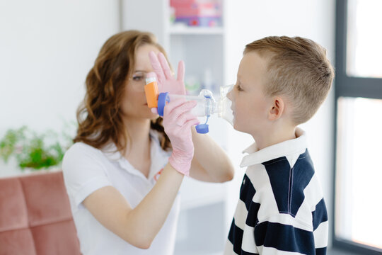 Boy with allergic asthma, inhaling his medication through spacer while sitting in doctors office
