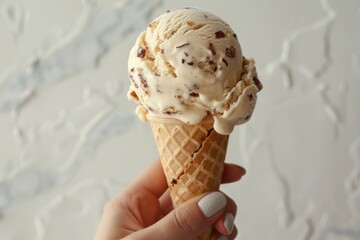 Hand of a woman holding a caramel pretzel ice cream cone on a white background, the mix of salty and sweet standing out