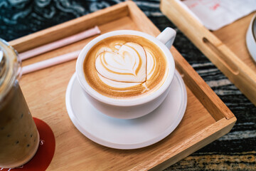 Heart shaped hot latte crafted in ceramic cup on wooden tray in coffee shop