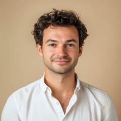 Fototapeta premium Young man with curly hair smiling warmly against a neutral background in a casual white shirt. Generative AI