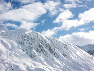 Obraz premium A snowy rocky mountain range and blue sky on a sunny near the ski pistes of a ski resort in the French or Swiss Alps in the winter