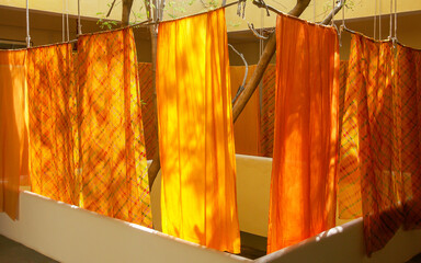 Various colorful orange sheets hanging out to dry in a courtyard of a house in the summer in India.