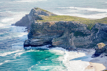 Rocky outcrop and sea cliffs next to the ocean in South Africa with a a small bay and beach in view