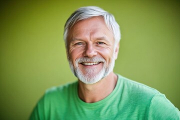Obraz premium A smiling mature Caucasian man with gray hair and beard wears a green T-shirt against a green background