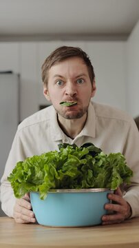 Funny hungry man vegan eating a green salad in big bowl at kitchen. Vertical video.