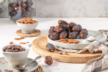 Medjool dates and almonds on a wooden board with a bowl of chocolate chunks and a bowl of almonds in the background, creating a rustic and healthy snack setup