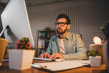 Fototapeta premium Focused man at his computer in a home office at night with notebooks around