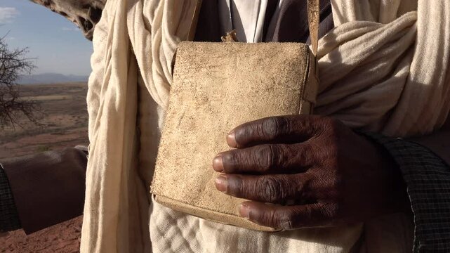 Senior priest holds leather pouch in remote mountainous desert location in Tigray region of Ethiopia
