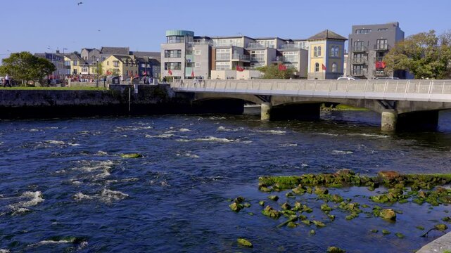 Corrib River in Galway Ireland - A peaceful river view reflecting sunlight, featuring a picturesque bridge and vibrant lush greenery