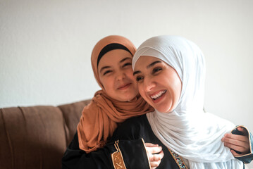 Happy Muslim family at home young mother and child daughter in hijab hug with love on sofa smiling and playing together for bonding with affection.