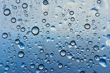 A close-up view of water droplets on a surface, showcasing a variety of sizes against a blue backdrop, creating a refreshing and tranquil ambiance.