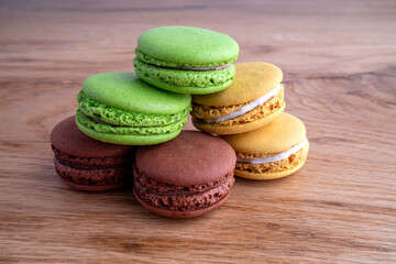 A colorful stack of macarons in vibrant green, yellow, and brown hues, beautifully arranged on a wooden surface, showcasing their delicate textures.