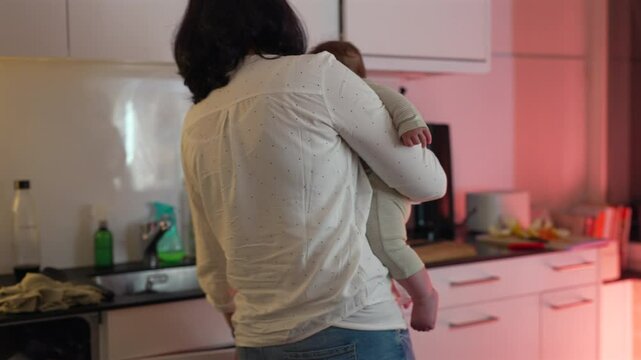 Mother multitasking while holding baby in kitchen, organizing and managing household tasks, focus on parenting and creating a nurturing family environment