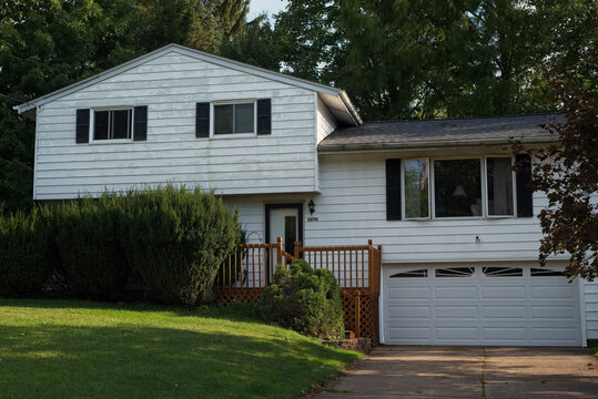 A split-level house with peeling paint on the aluminum siding and overgrown bushes in front