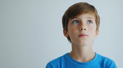 Contemplative young boy with light brown hair wearing a vibrant blue shirt gazing upward against a soft white background, evoking introspection and curiosity.
