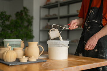 Close-up of a potter's hands glazing a ceramic mug. 