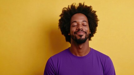 Calm adult African American man with curly hair wearing purple t-shirt meditating with closed eyes on vibrant yellow studio background, conveying tranquility and relaxation.