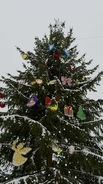 A tall Christmas tree adorned with colorful ornaments, lights, and a star topper. The branches are lightly covered in snow, creating a festive and wintry atmosphere