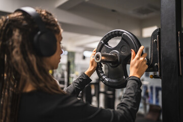 young woman adjusting weight plate on gym equipment wearing headphones