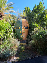 Unique Large Artistic Mask Surrounded by Lush Greenery in a Vibrant Garden Setting