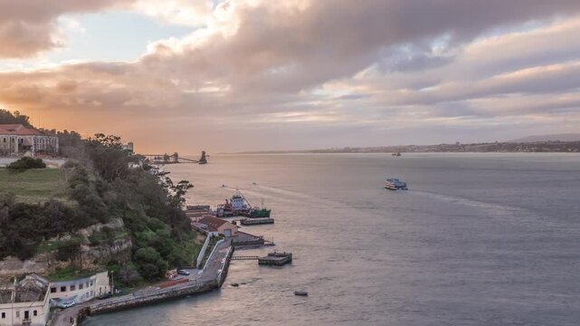 Aerial timelapse panorama from a hill near Porto Brandao Ferry Station on the Tagus River in Lisbon. Dramatic sunset with colorful clouds, a ship floating on water and Terminal in background