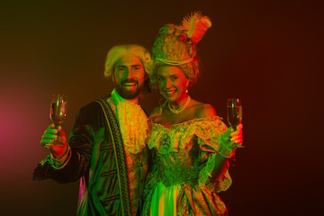 Elegant couple in elaborate vintage attire toasting with glasses in dim lighting at a themed...