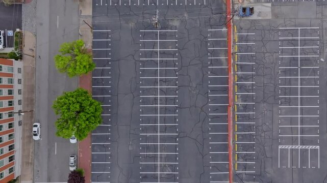 A beautiful overhead view from a rotating drone UAS of a large urban city vacant parking lot with black asphalt and white stripes and parking space. Overhead nadir view from descending aerial drone.