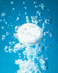 Fototapeta premium Dissolving white tablet creates bubbles in vivid blue water background
