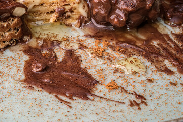 A close-up view of dessert with smeared chocolate mess. Crumbled cookies, and a dusting of cocoa powder. Rich textures and colors of chocolate.