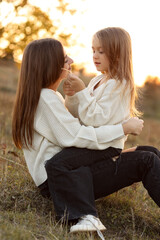 Fototapeta premium Family day, mother's day. Happy smiling young mom and adorable child daughter soft hugging, kissing and spending time together at autumn on sunset. Idyllic family having fun outdoors on fall holiday.