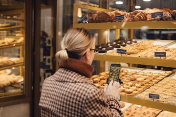 Middle age traveler woman recording video on phone with traditional Portuguese desserts Pastel de nata in the window of a bakery in Lisbon. UGC Vlogger. Part of a series