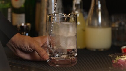 Cropped closeup hand bartender stirring mixed ingredients alcohol liquor syrup into mixing glass with cube ice prepared Old fashioned cocktail tasting showcasing nightlife mixology at bar. Vinosity.